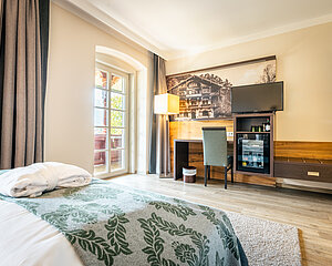 Gemütliches Hotelzimmer mit Bett, Schreibtisch, Fernseher, Minibar und Zugang zum Balkon bei Tageslicht