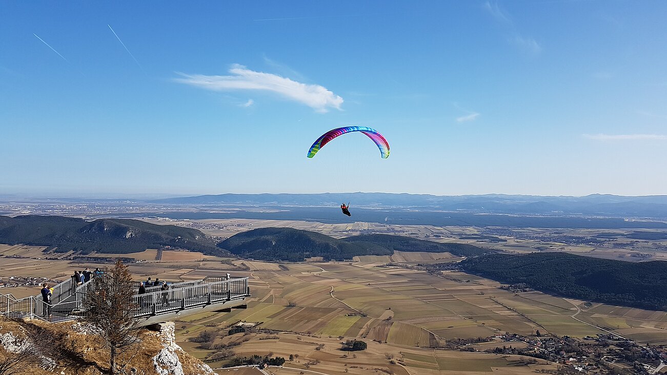 Gleitschirmflieger über malerischem Tal mit Aussichtsplattform und fernen Bergen