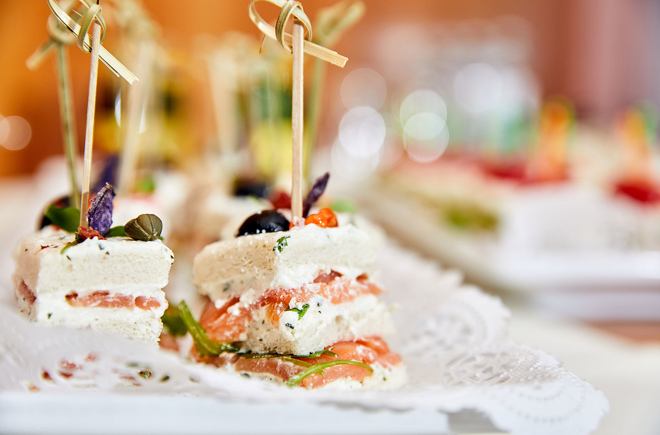 Gourmet Häppchen mit Räucherlachs, Frischkäse und Kräutern auf weißer Servierplatte