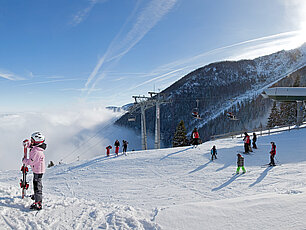 Skifahrer und Snowboarder im sonnigen Bergskigebiet mit Skilift und verschneiten Pisten