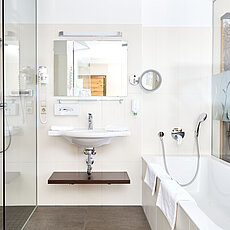 Modern hotel bathroom with glass shower, bathtub, sink and wall-mounted amenities