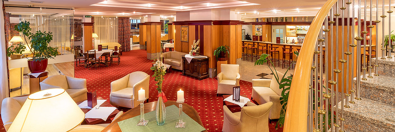 Elegante Hotellobby mit rotem Teppich, beigen Sesseln und geschwungener Treppe