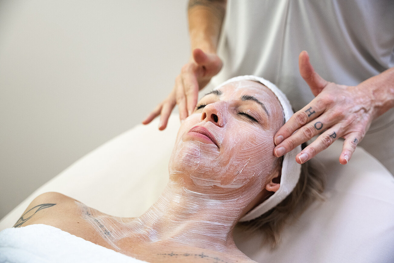 Woman receiving facial treatment with white cream mask at beauty spa