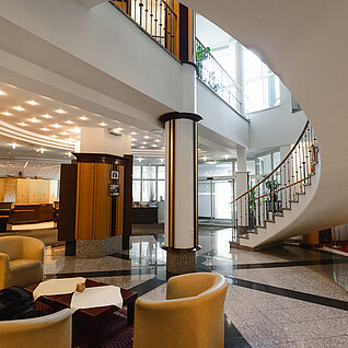 Moderne Hotellobby mit beigen Stühlen, Marmorboden und Wendeltreppe