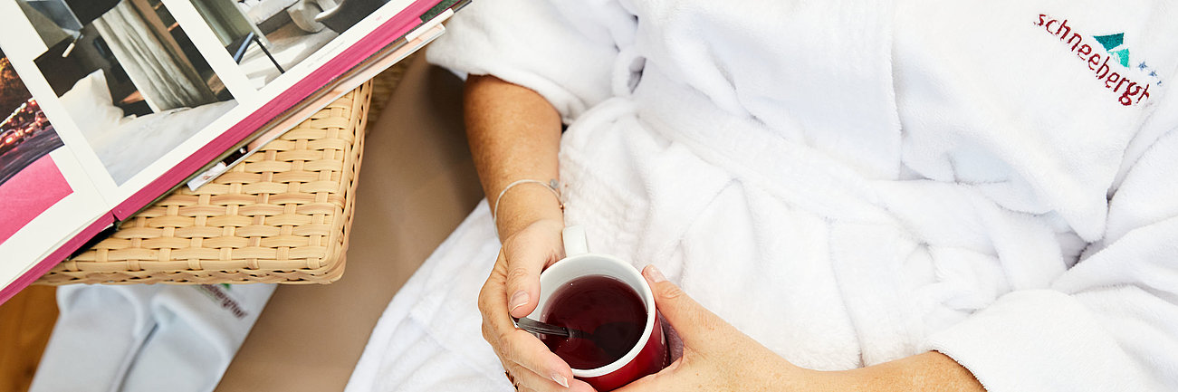 Frau entspannt im Spa-Bademantel mit Kräutertee und Hotelbroschüre im Schneeberg-Resort