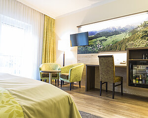 Modern hotel room with green armchairs, desk, minibar and mountain landscape wall art
