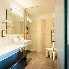 Modern hotel bathroom with walk-in shower, large sink counter, and wall-mounted hairdryer