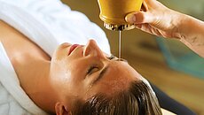 Ayurvedische Kopfmassage mit Öl, das bei einer Spa-Behandlung auf die Stirn tropft