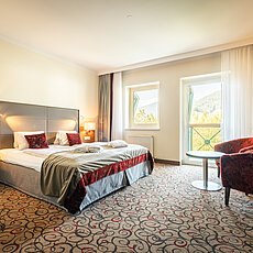 Bright hotel room with double bed, red accents, armchairs and mountain view