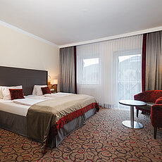 Modern hotel room with double bed, red armchairs, and balcony access through glass doors