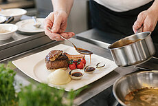 Koch richtet Gourmet-Rinderfilet mit Kartoffelpüree, Cherrytomaten und Zwiebelsauce an