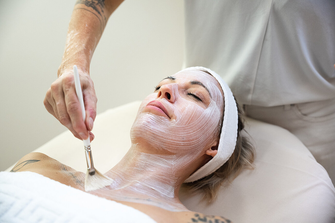 Woman receiving facial treatment with brush-applied cream at a spa