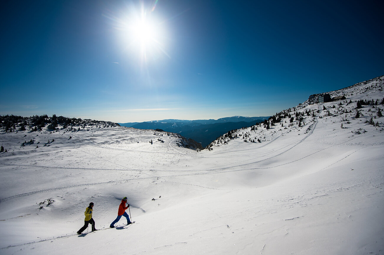 Zwei Personen beim Schneeschuhwandern an einem sonnigen Wintertag in verschneiter Berglandschaft
