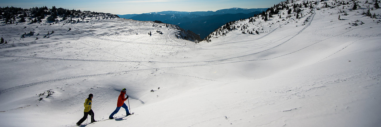 Two people snowshoeing uphill on a sunny winter day in a snowy mountain landscape