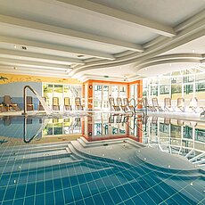 Helles Hotel-Innenschwimmbad mit Liegestühlen, Oberlicht und Wasserfall