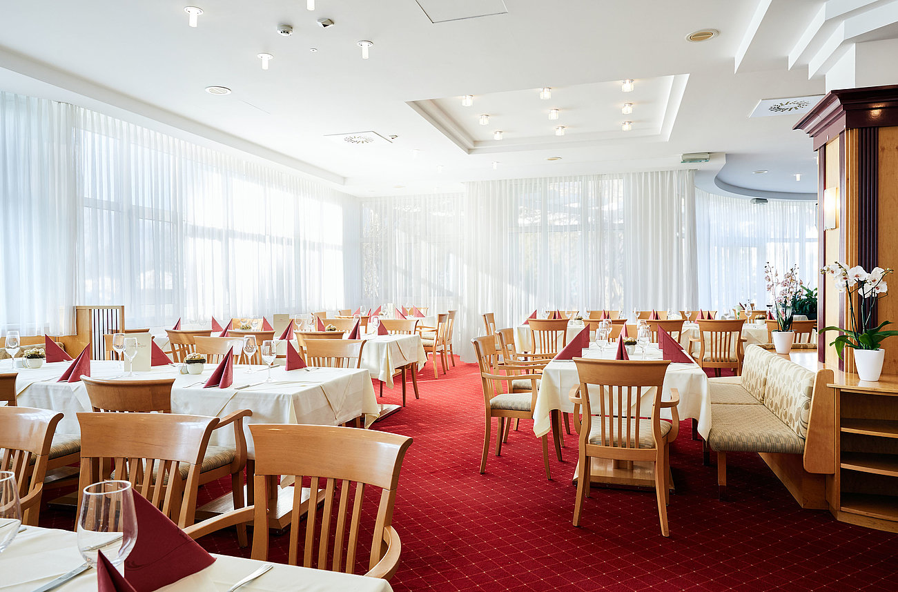 Bright restaurant interior with wooden furniture, white tablecloths, and red napkins