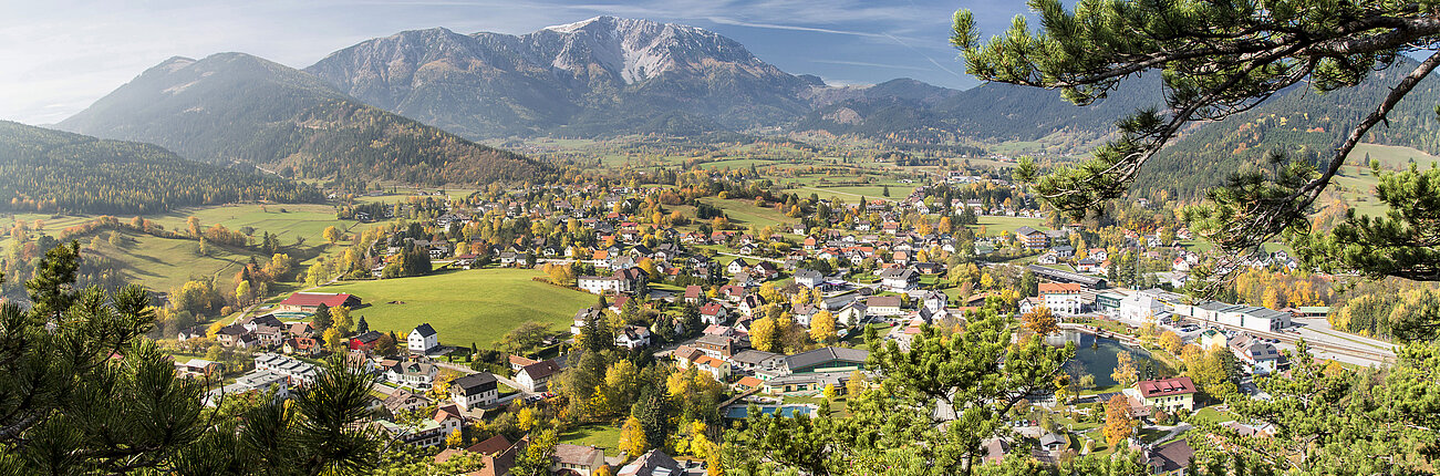 Panoramablick auf alpines Dorf mit bunten Herbstbäumen und Bergkulisse