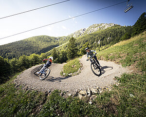 Zwei Mountainbiker auf einem kurvigen Schotterweg in einer malerischen Berglandschaft