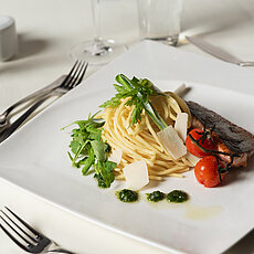 Gourmet-Spaghetti mit gegrilltem Lachs, Kirschtomaten, Rucola und Pesto auf weißem Teller