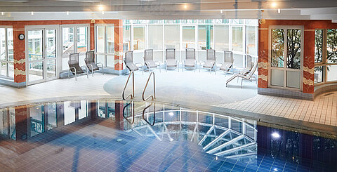 Innenbereich mit Spa-Pool, Liegestühlen und großen Fenstern bei Tageslicht