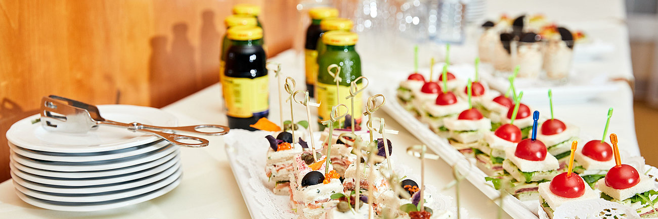 Catering-Tisch mit verschiedenen Häppchen, Sandwiches, Gebäck, Saftflaschen und Wasser
