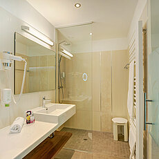 Modern hotel bathroom with walk-in shower, wall-mounted sink, and vanity mirror with LED light