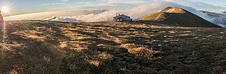 Berghütte auf alpiner Wiese im Sonnenaufgang mit Panoramablick und Wolken