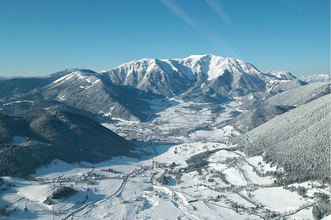 Schneebedecktes Alpen-Tal mit bewaldeten Bergen unter klarem blauen Himmel