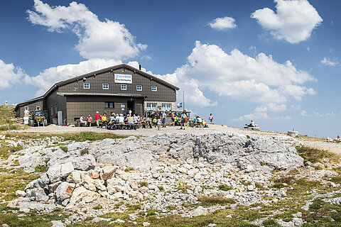 Berghütte Fischerhütte mit Wanderern im Freien auf felsigem Alpengelände bei Sonnenschein