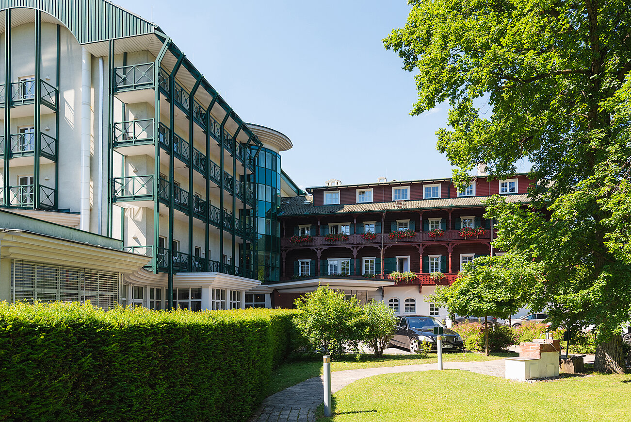 Hotel mit Balkonen, grünen Hecken und großem Baum unter klarem blauen Himmel