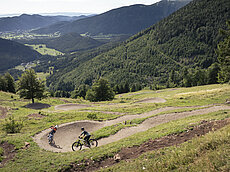 Zwei Radfahrer auf einem Bergpfad mit üppigem Wald und Talblick