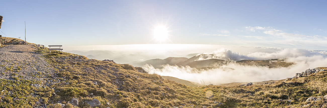 Berghütte auf felsigem Plateau mit Panoramablick auf Sonnenaufgang über Alpenwolken