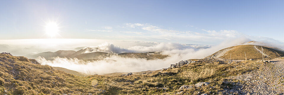 Berghütte auf felsigem Plateau mit Panoramablick auf Sonnenaufgang über Alpenwolken