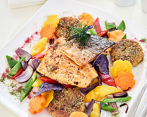 Grilled salmon fillet with colorful vegetables and quinoa patties on a white plate