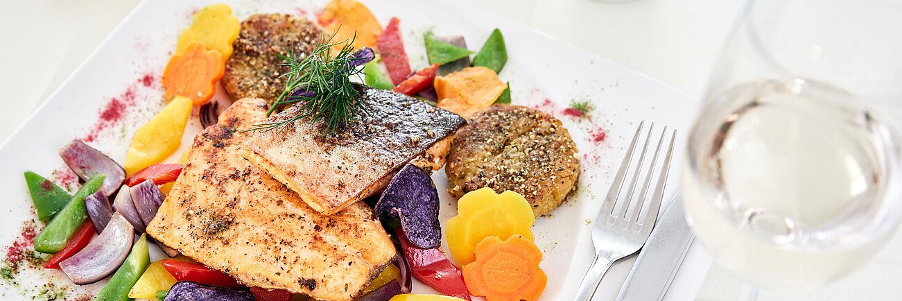 Grilled salmon fillet with colorful vegetables and quinoa patties on a white plate