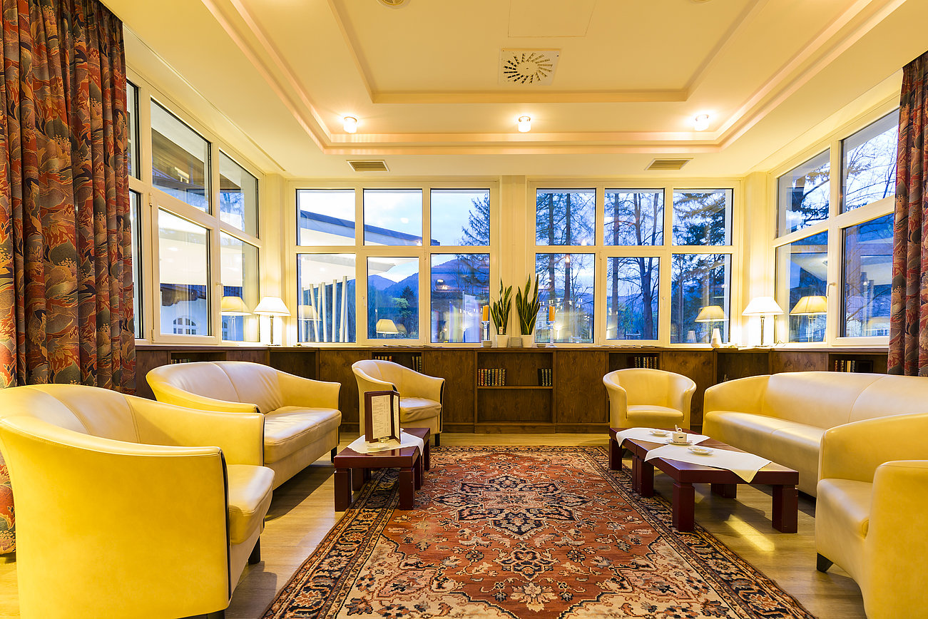 Gemütliche Hotellounge mit gelben Sesseln, großen Fenstern und gemustertem Teppich