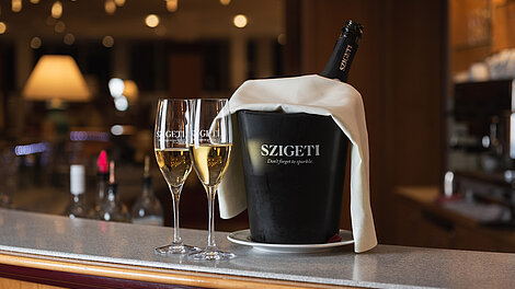 Zwei Champagnergläser und Szigeti-Sektflasche im Eisbehälter auf der Bartheke