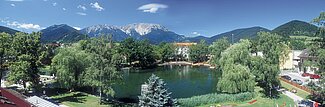 Mountain village with lake surrounded by trees and alpine peaks under blue sky