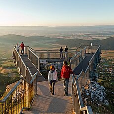 Touristen auf einer erhöhten Bergplattform mit Blick auf das Tal bei Sonnenuntergang