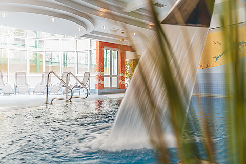 Innenpool mit Wasserfall und Sonnenliegen an großen Fenstern