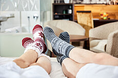 Paar entspannt in gemütlichen Wintersocken auf dem Bett im Hotelzimmer