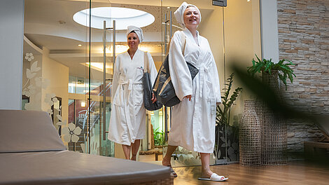 Zwei Frauen in Bademänteln und Handtüchern betreten den Wellness-Spa-Ruhebereich