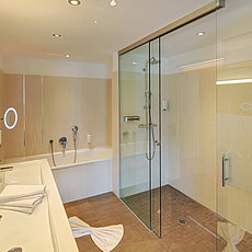 Modernes Hotelbad mit begehbarer Glasdusche, Badewanne und Doppelwaschbecken