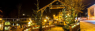 Festlich beleuchtete Holzbrücke und Weihnachtsbäume in einer Stadt bei Nacht