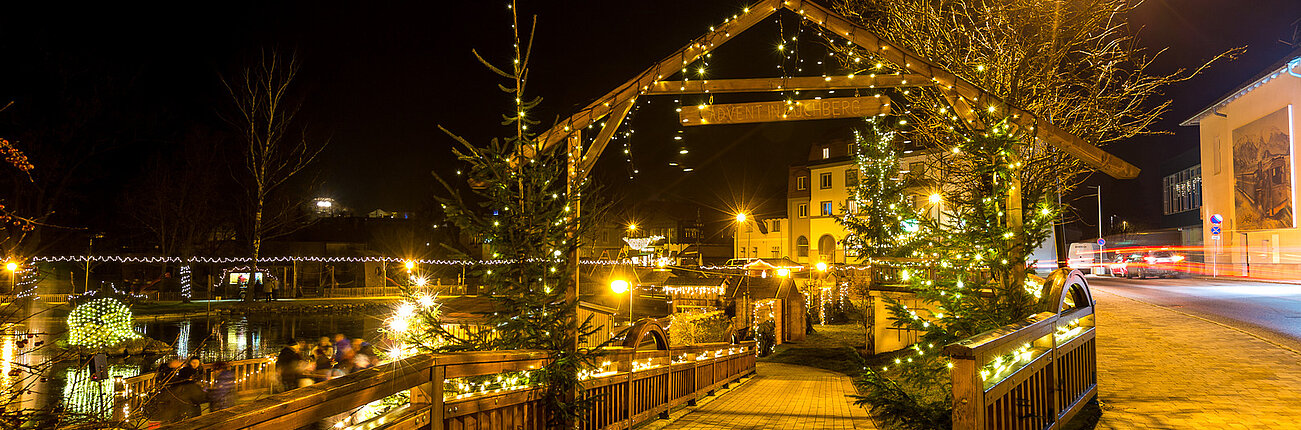 Festlich beleuchtete Holzbrücke und Weihnachtsbäume in einer Stadt bei Nacht