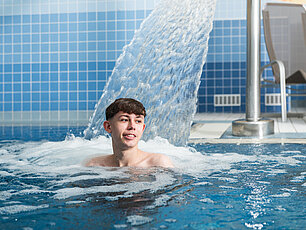 Junger Mann entspannt im Innen-Whirlpool mit Wasserstrahl und blauer Fliesenwand