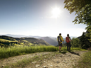 Zwei Wanderer mit Rucksäcken auf einem Pfad mit Blick auf sonnige Hügel im Schwarzwald