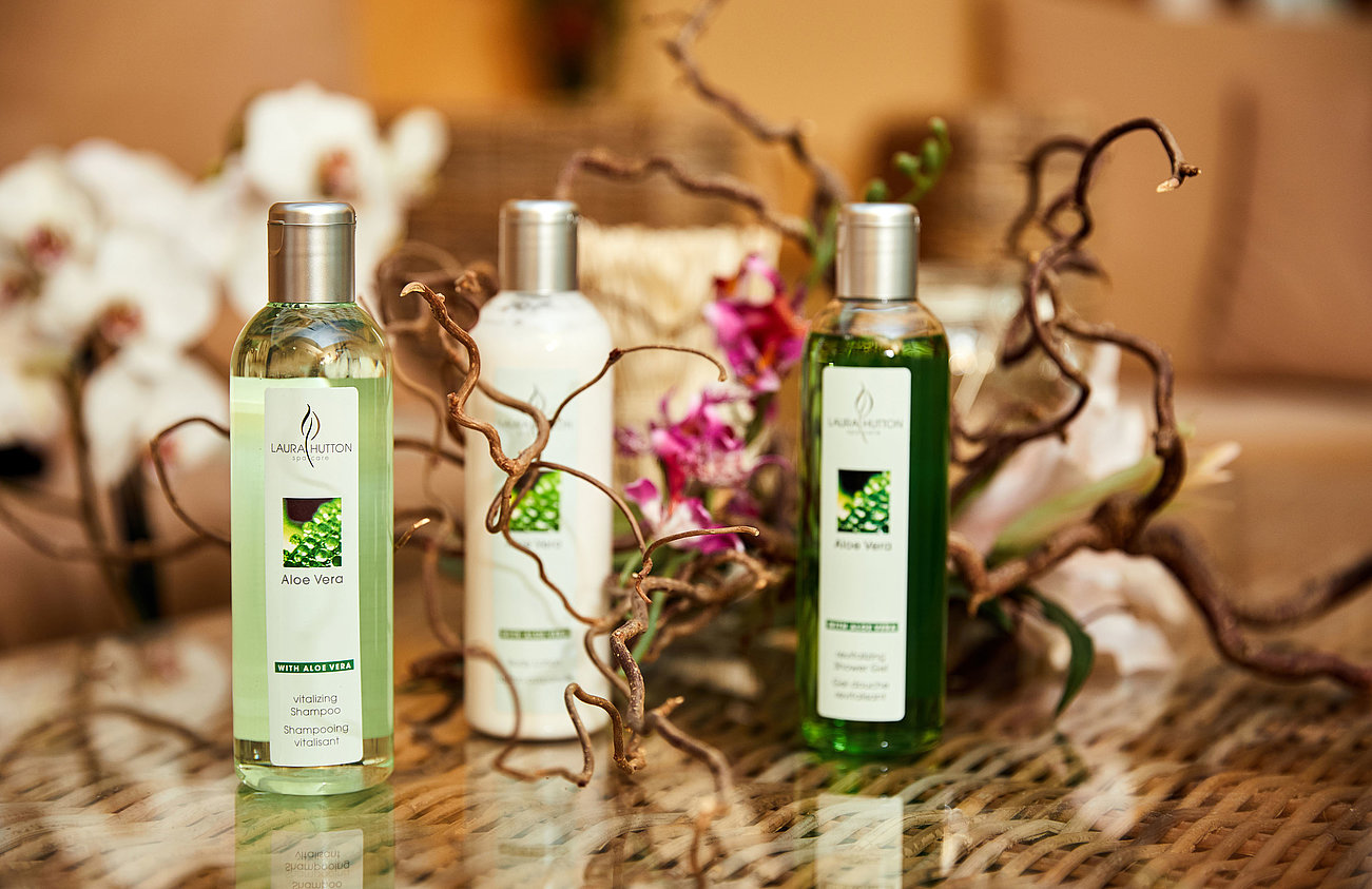 Laura Hutton Aloe Vera Shampoo- und Duschgelflaschen auf Glastisch mit Blumendekoration
