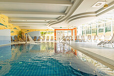 Innenpool mit Wasserfall und Liegestühlen in heller Spa-Landschaft