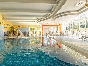 Innenpool mit Wasserfall und Liegestühlen in heller Spa-Landschaft